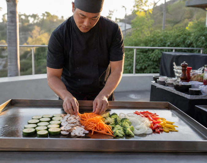 Fresh vegetables and mushrooms arranged on a hibachi grill before cooking