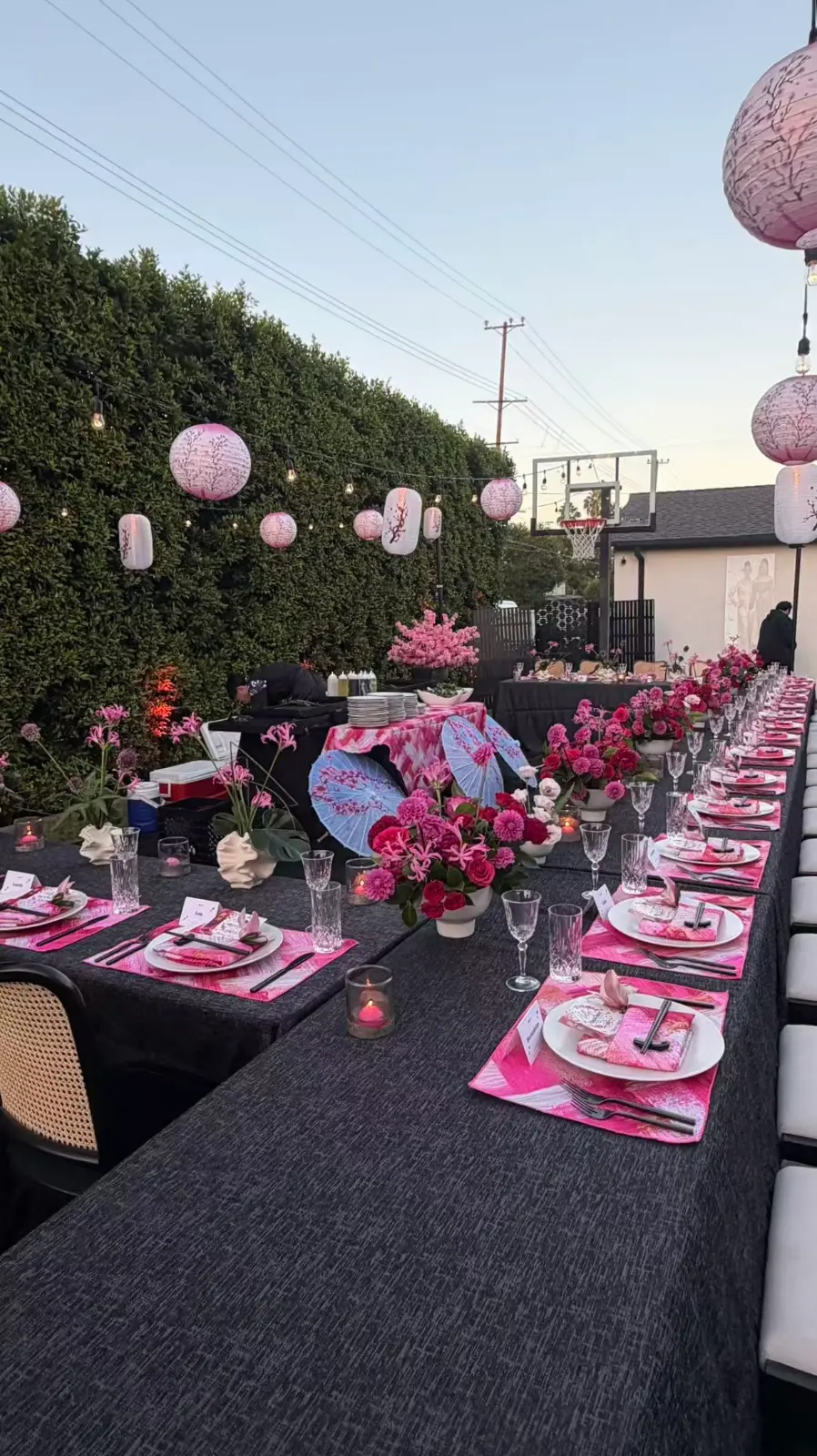 Alt: Outdoor hibachi event setup with a long dining table, pink floral decorations, lanterns, and place settings.
