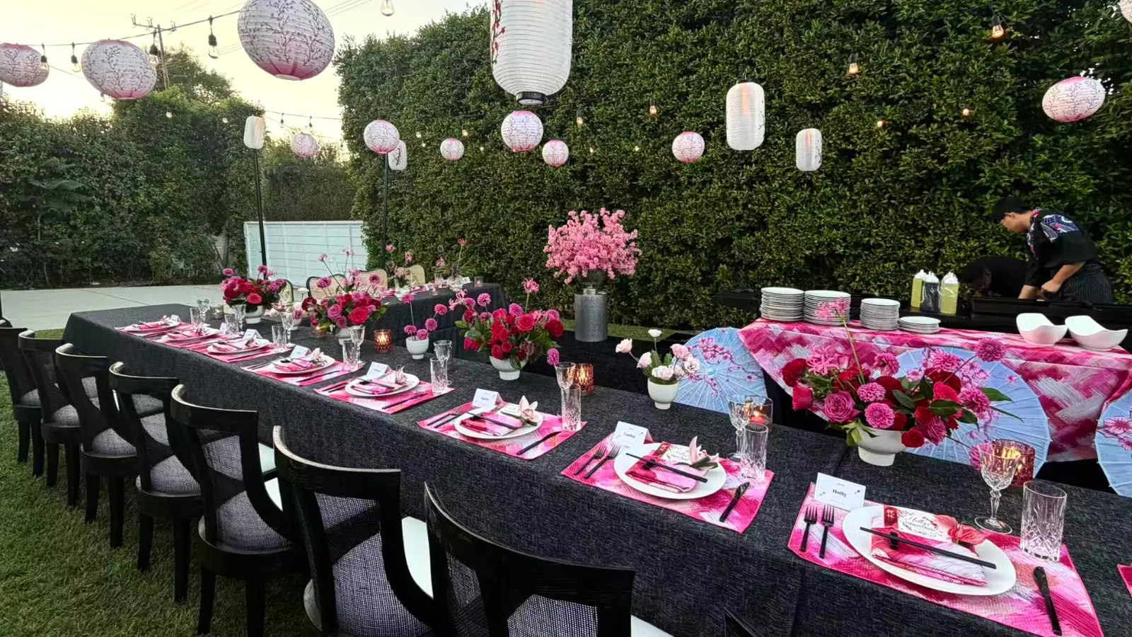 Outdoor dining tables with pink flowers and lanterns at a private event.