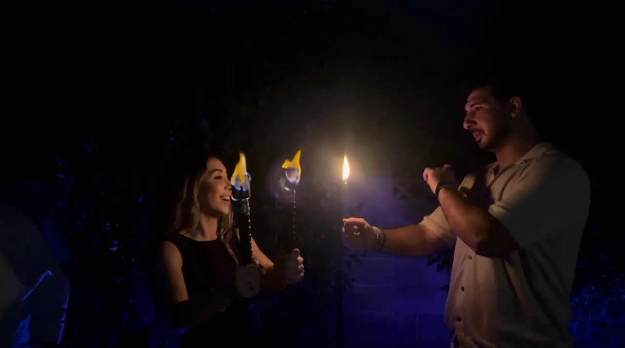 Guests smile and interact beside flaming torches at an outdoor nighttime event.